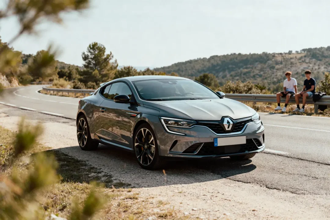 Voiture grise Renault sur route sinueuse, collines arides, deux personnes assises sur glissière de sécurité.