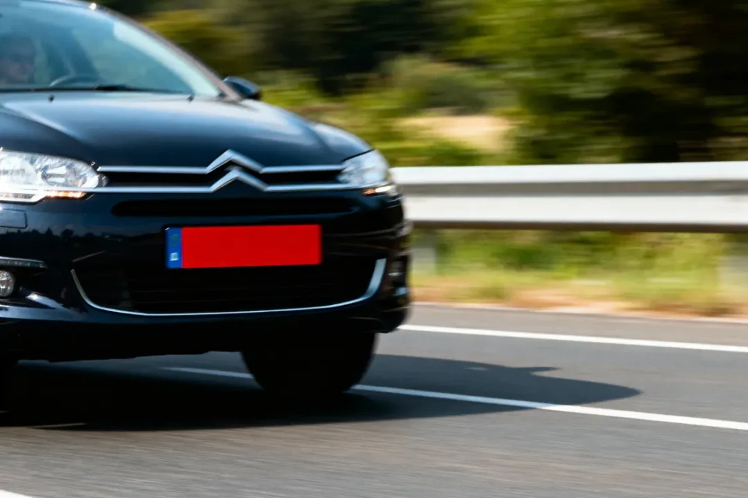 Voiture noire Citroën sur route avec glissière de sécurité, plaque floue, végétation en arrière-plan.