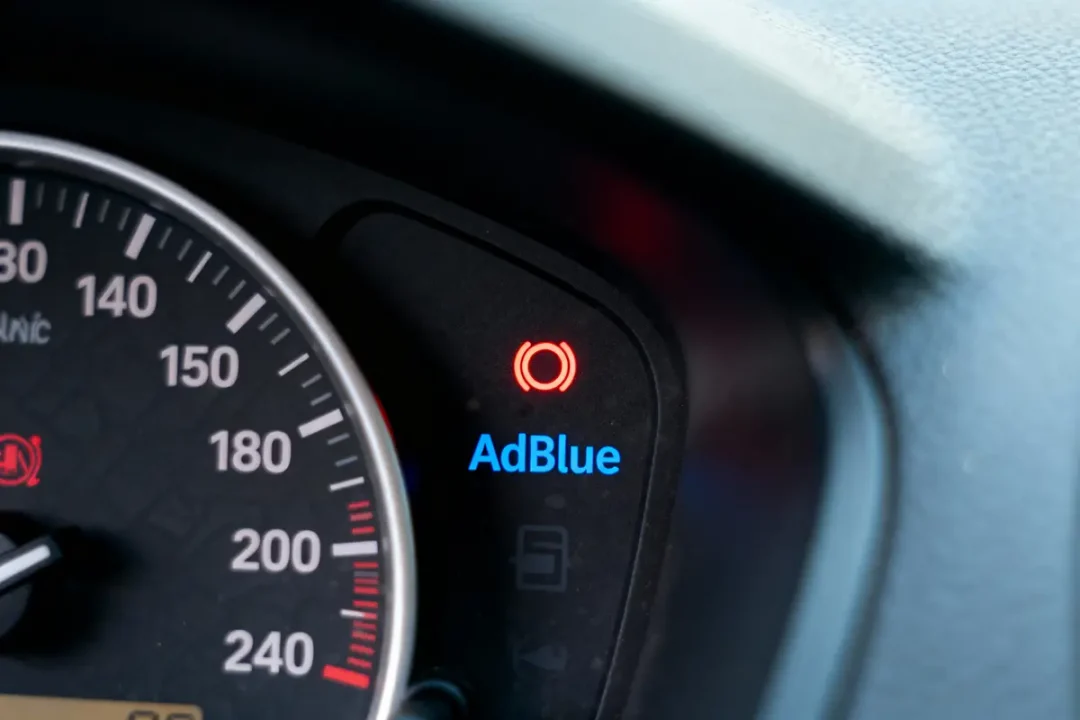 Tableau de bord de voiture avec voyant AdBlue illuminé et tachymètre partiellement visible.