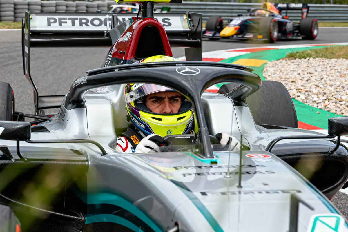 Pilote de course en action dans une Formule 1, concentré, portant un casque, d'autres voitures en arrière-plan.