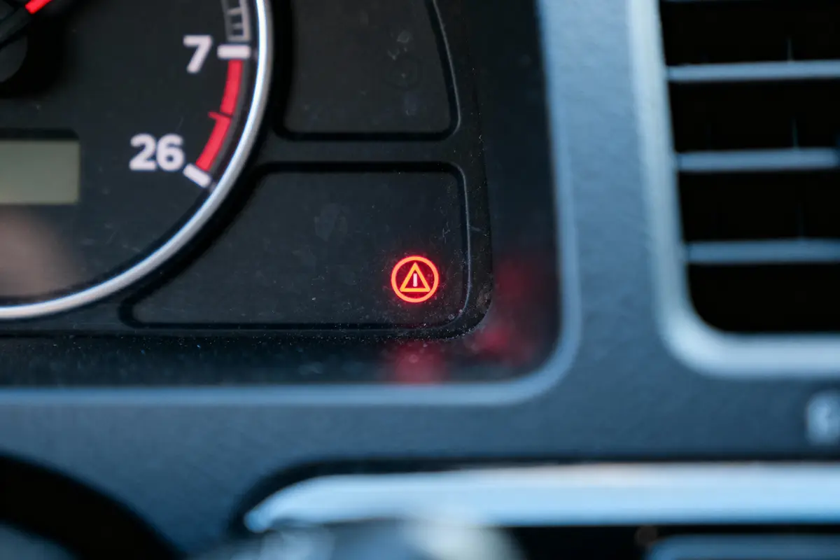 Voyant rouge allumé sur le tableau de bord d'une voiture, symbole triangulaire entouré.