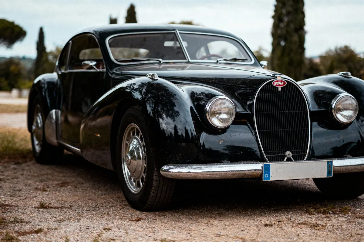 Voiture noire ancienne stationnée, Bugatti vintage, extérieur, journée, arbres en arrière-plan flou.