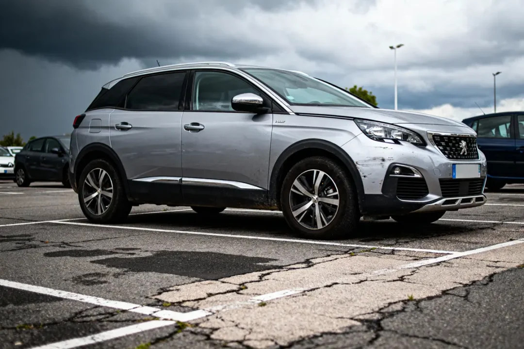 SUV gris stationné sur un parking sous un ciel nuageux menaçant. Autres voitures visibles en arrière-plan.