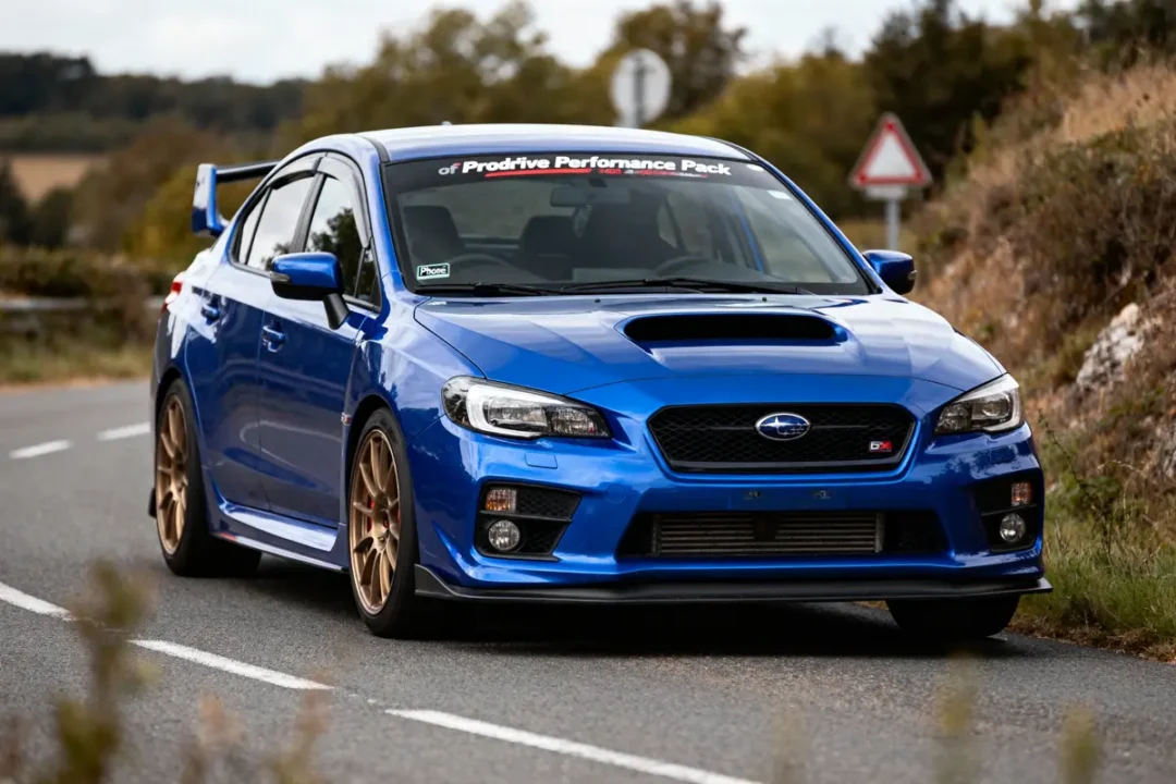 Voiture bleue sportive Subaru sur route de campagne, autocollant "Prodrive Performance Pack", jantes dorées, paysage naturel.