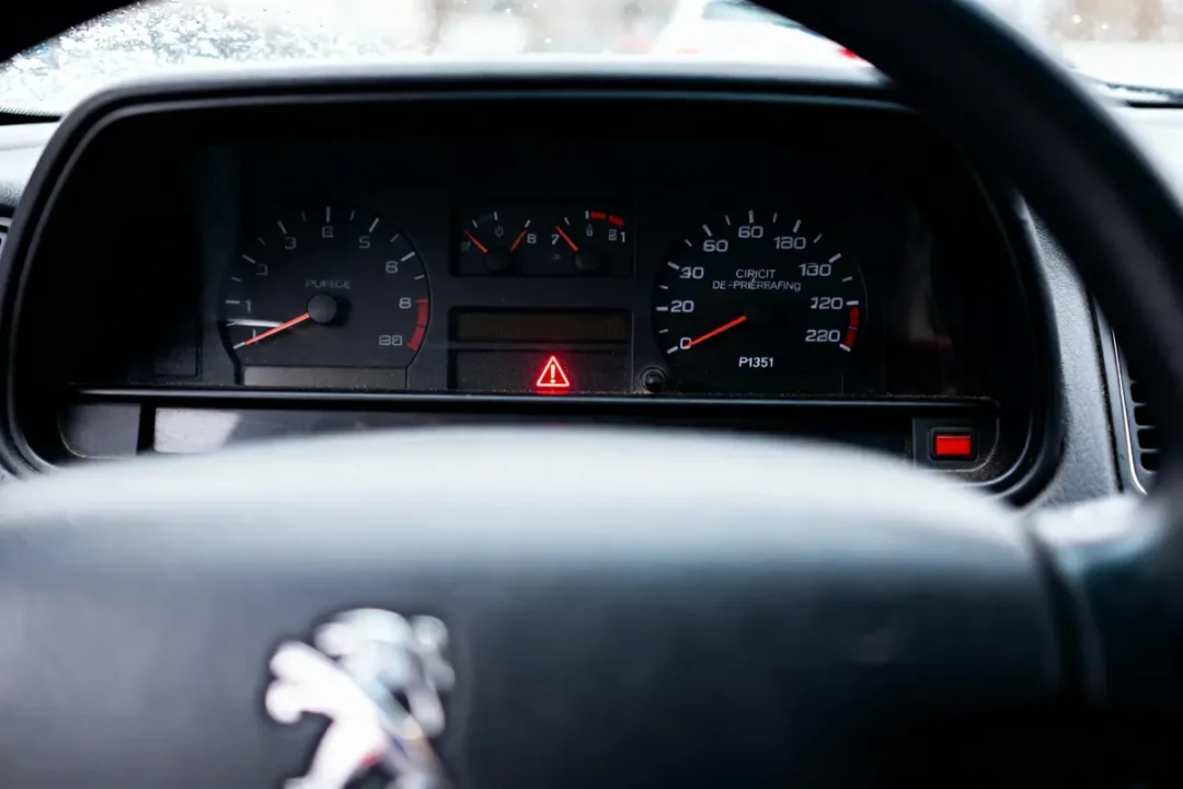 Tableau de bord de voiture, jauges et voyants allumés, logo Peugeot sur le volant.