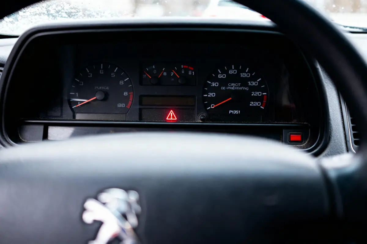 Tableau de bord de voiture, jauges et voyants allumés, logo Peugeot sur le volant.