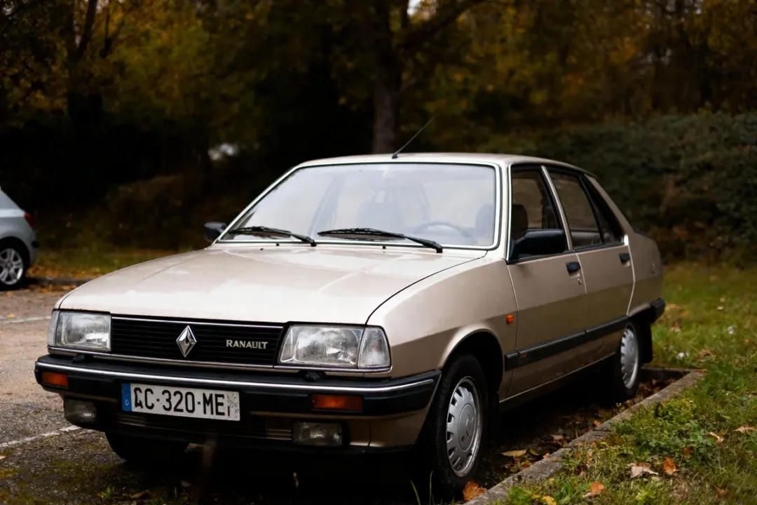 Voiture Renault beige garée, plaque CC-320-ME, devant feuillage automnal, angle avant gauche.