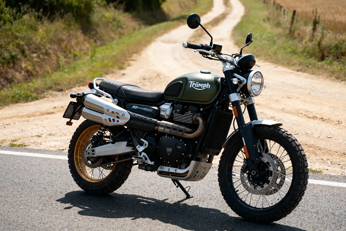Moto verte Triumph stationnée sur une route de campagne ensoleillée avec chemins de terre environnants.