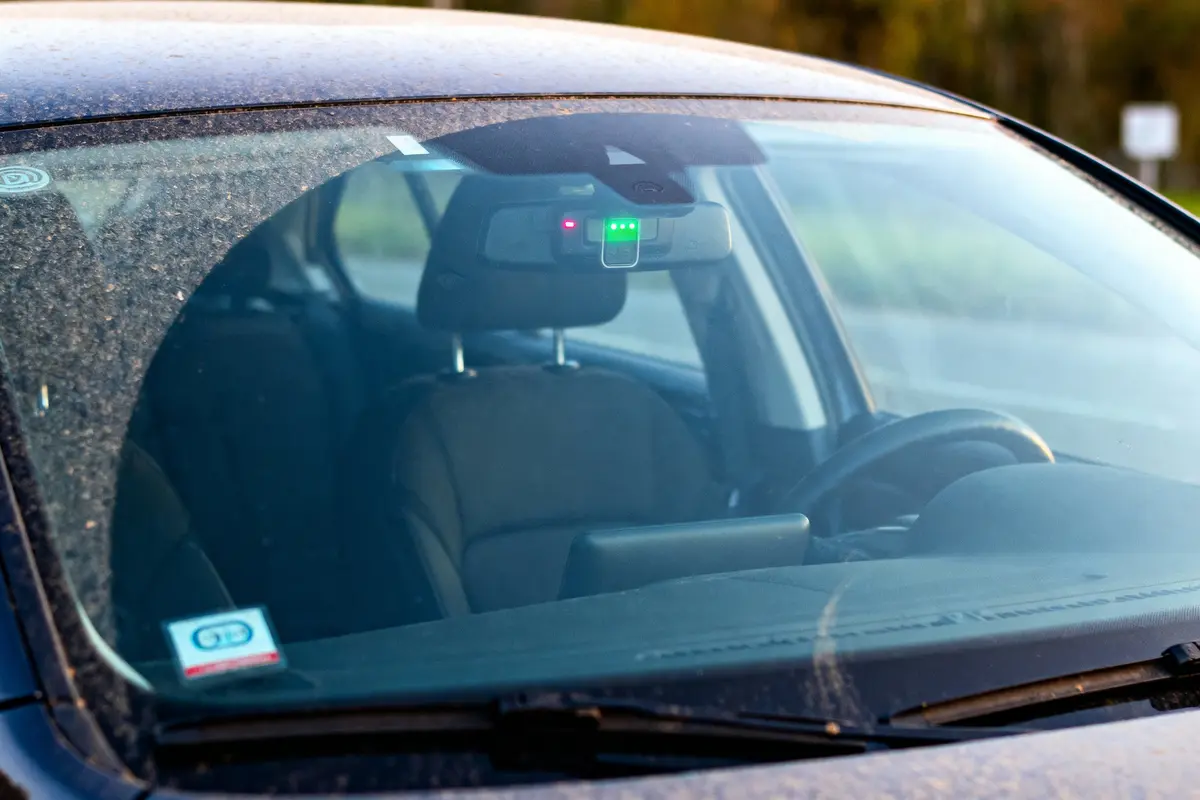 Vue intérieure d'une voiture, pare-brise avec capteur lumineux et carte de stationnement visible.