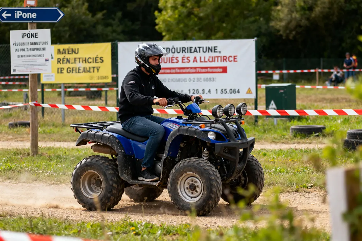 Homme conduisant un quad bleu sur un parcours extérieur délimité par ruban de sécurité. Panneaux en arrière-plan.