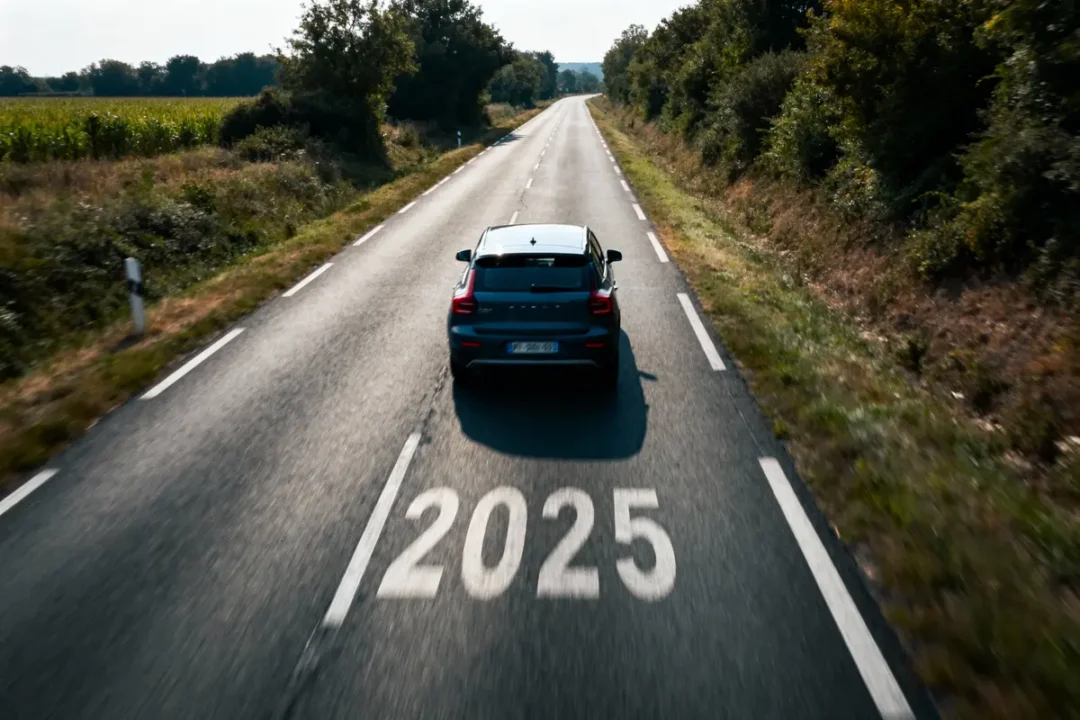 Voiture sur route bordée d'arbres avec "2025" peint sur l'asphalte. Paysage champêtre, ciel bleu.
