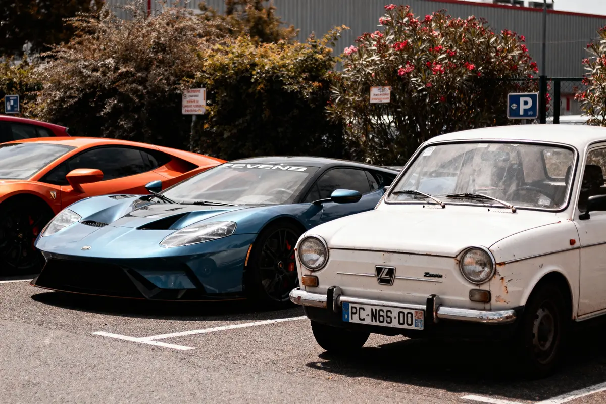 Trois voitures de sport colorées garées, une blanche ancienne au premier plan.
