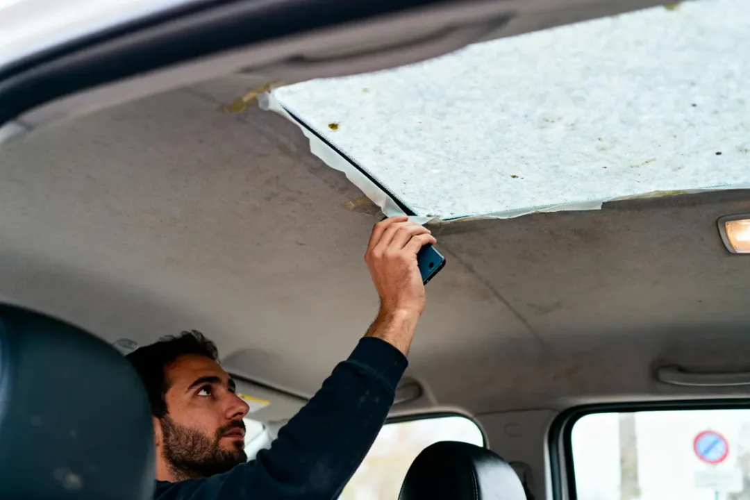 Homme répare le plafond intérieur d'une voiture en utilisant un smartphone comme outil ou lumière.