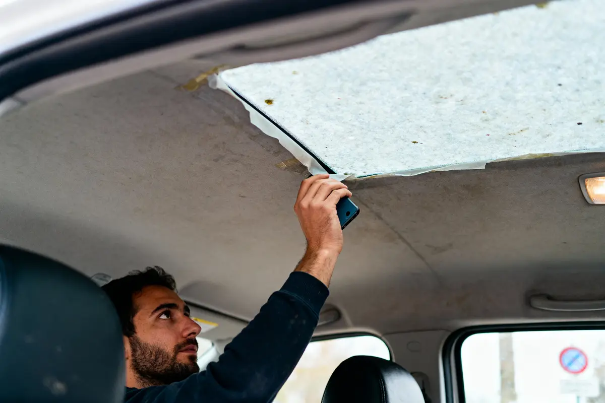 Homme répare le plafond intérieur d'une voiture en utilisant un smartphone comme outil ou lumière.