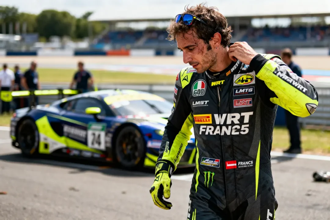 Pilote de course en combinaison noire près d'une voiture de course sur un circuit, nettoyant son visage.