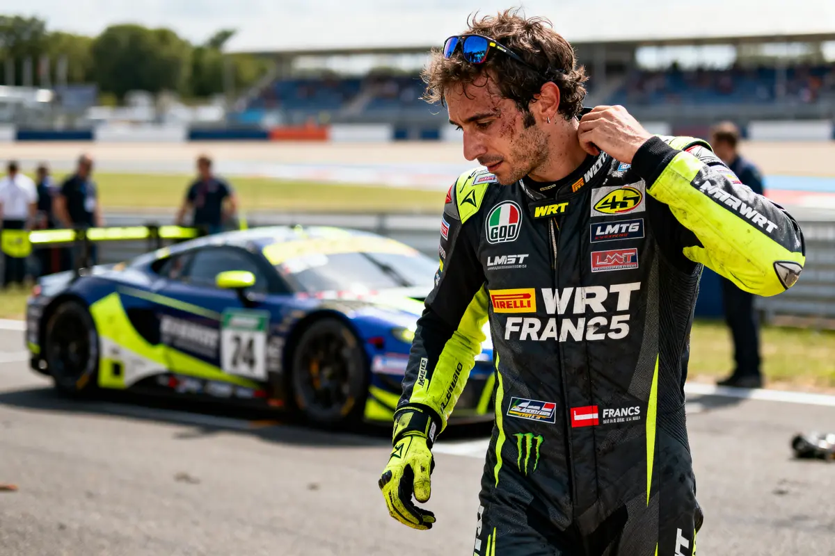 Pilote de course en combinaison noire près d'une voiture de course sur un circuit, nettoyant son visage.