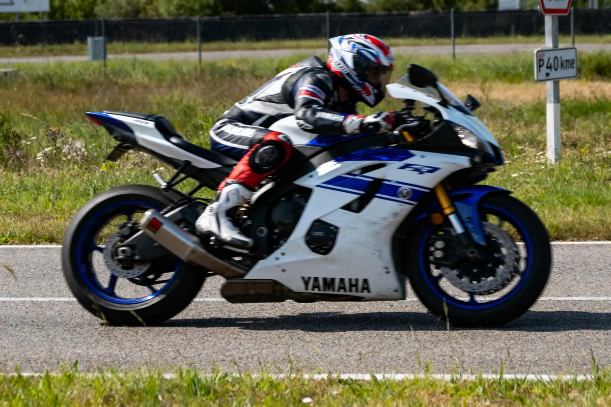 Motard en combinaison, sur Yamaha R1, roulant sur circuit. Vitesse indiquée par panneau "P 40 km". Jardin environnant.