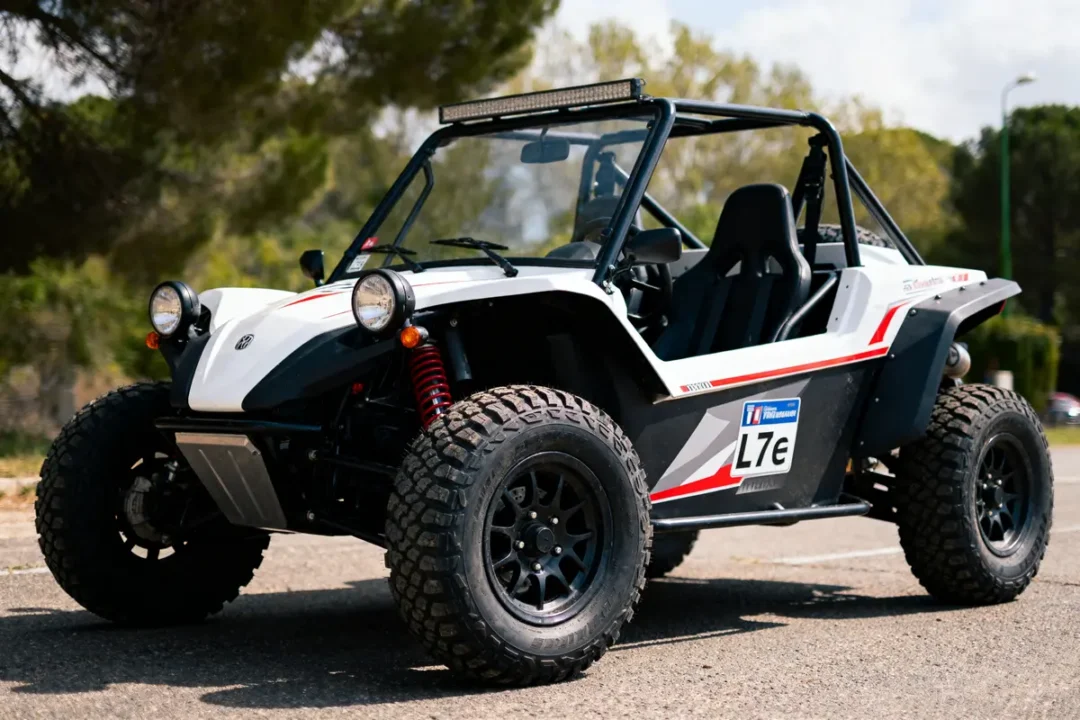 Buggy blanc et noir, pneus tout-terrain, stationné sur route pavée, entouré de végétation, en plein jour.