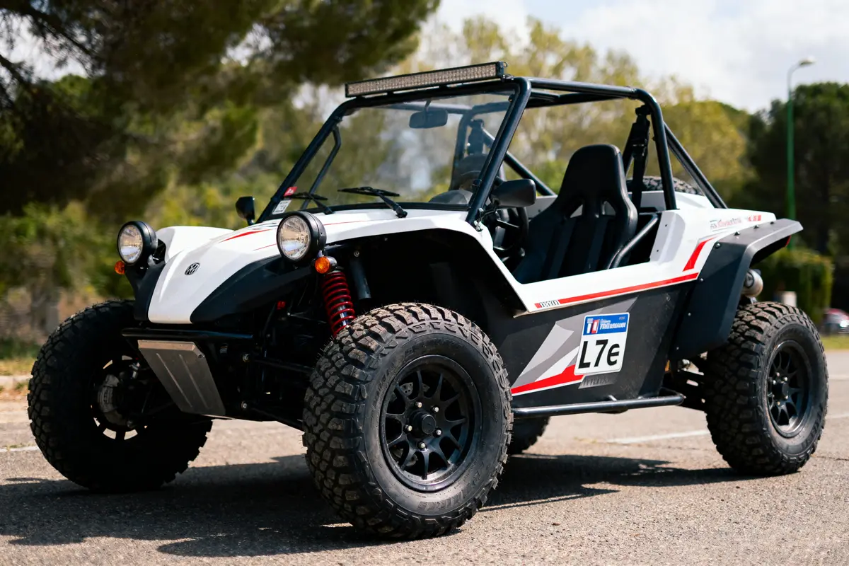 Buggy blanc et noir, pneus tout-terrain, stationné sur route pavée, entouré de végétation, en plein jour.