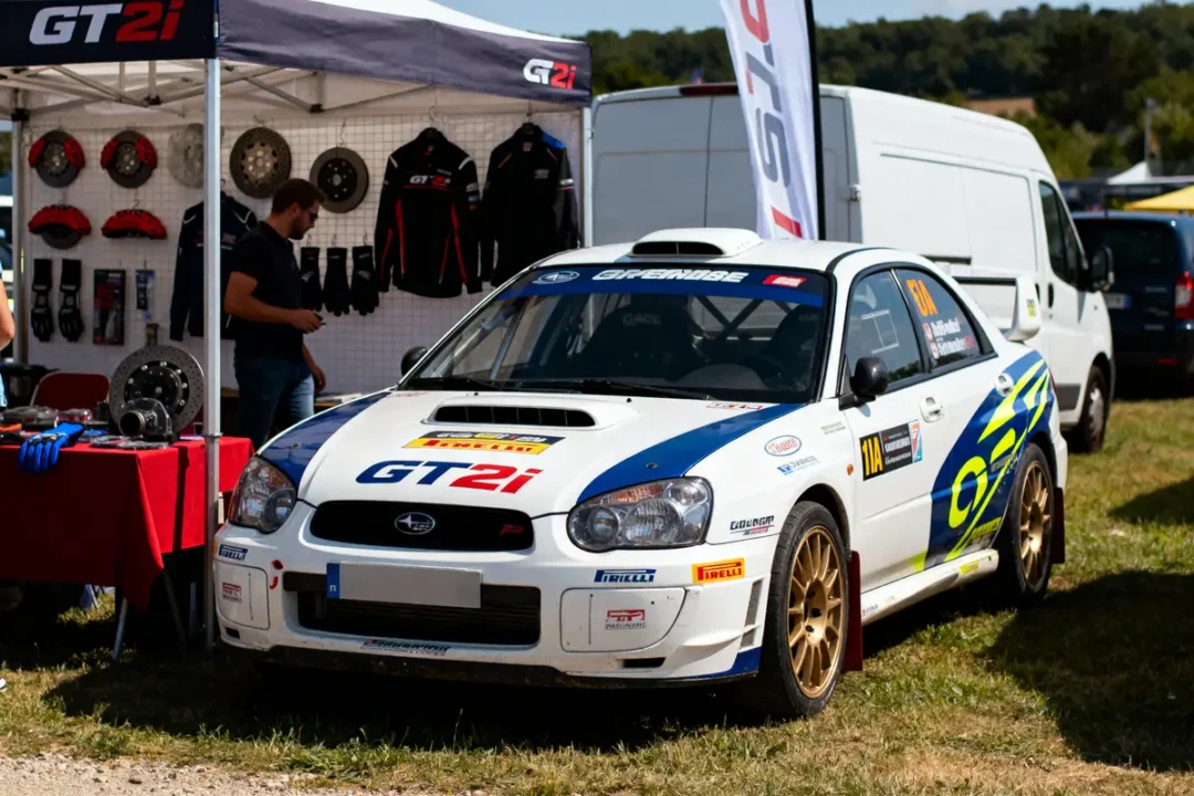 Voiture de course Subaru blanche exposée devant un stand GT2i avec accessoires automobiles.