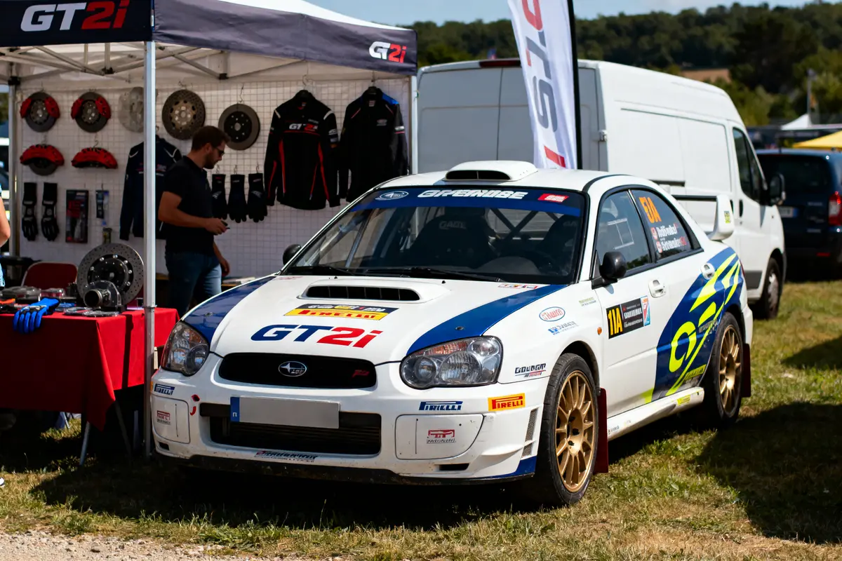 Voiture de course Subaru blanche exposée devant un stand GT2i avec accessoires automobiles.