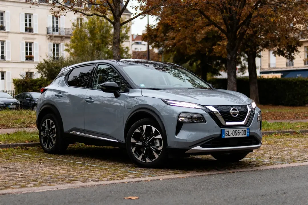 SUV gris garé dans la rue, avec bâtiments et arbres d'automne en arrière-plan. Plaque d'immatriculation visible.