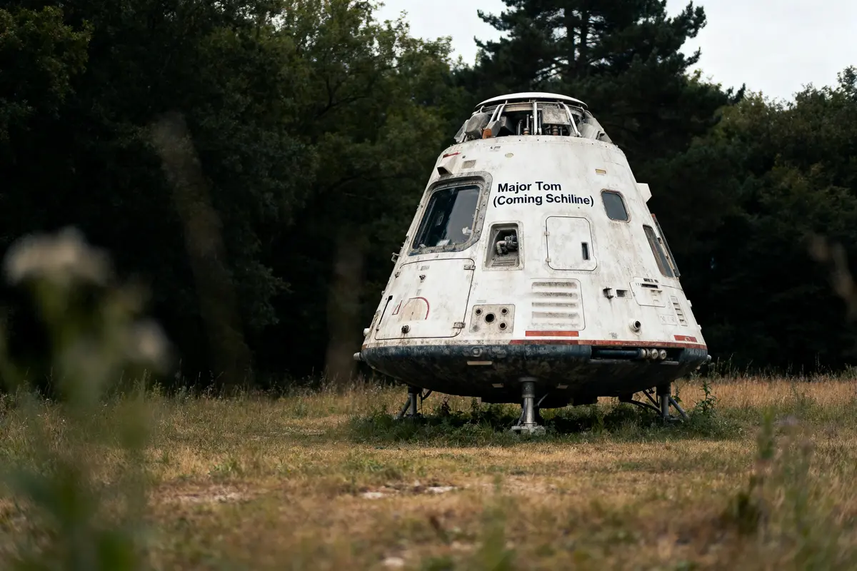 Capsule spatiale vintage "Major Tom" sur pelouse, entourée d'arbres, avec apparence usée épousant l'environnement naturel.