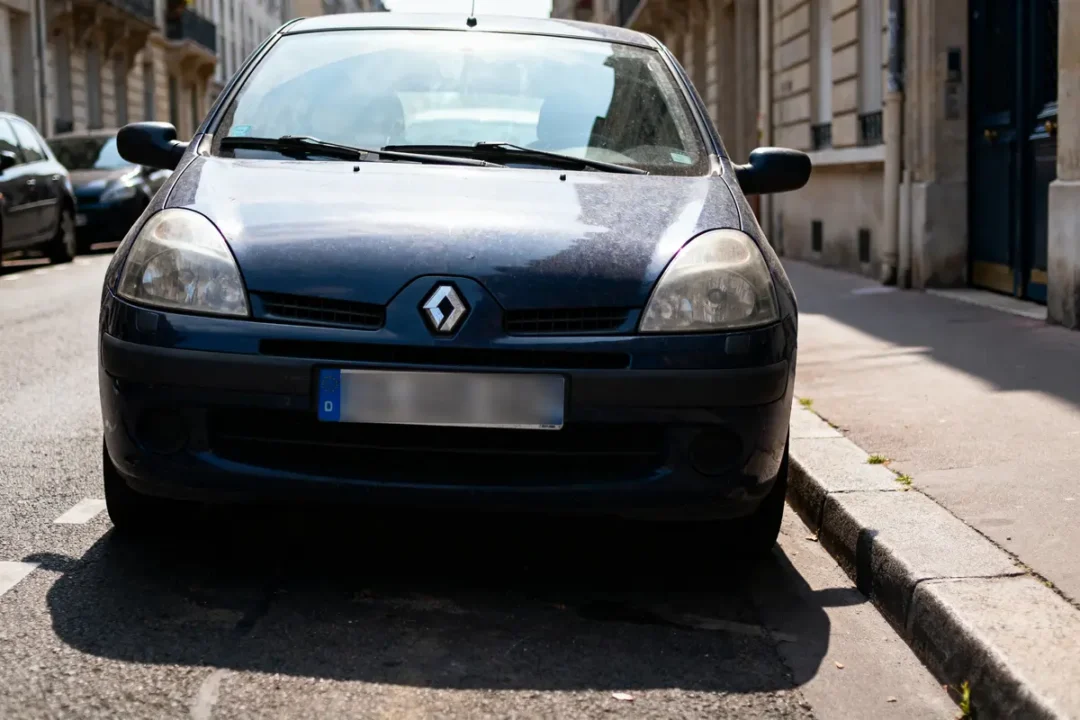 Voiture bleue Renault garée dans une rue urbaine, bâtiments en arrière-plan, jour ensoleillé.