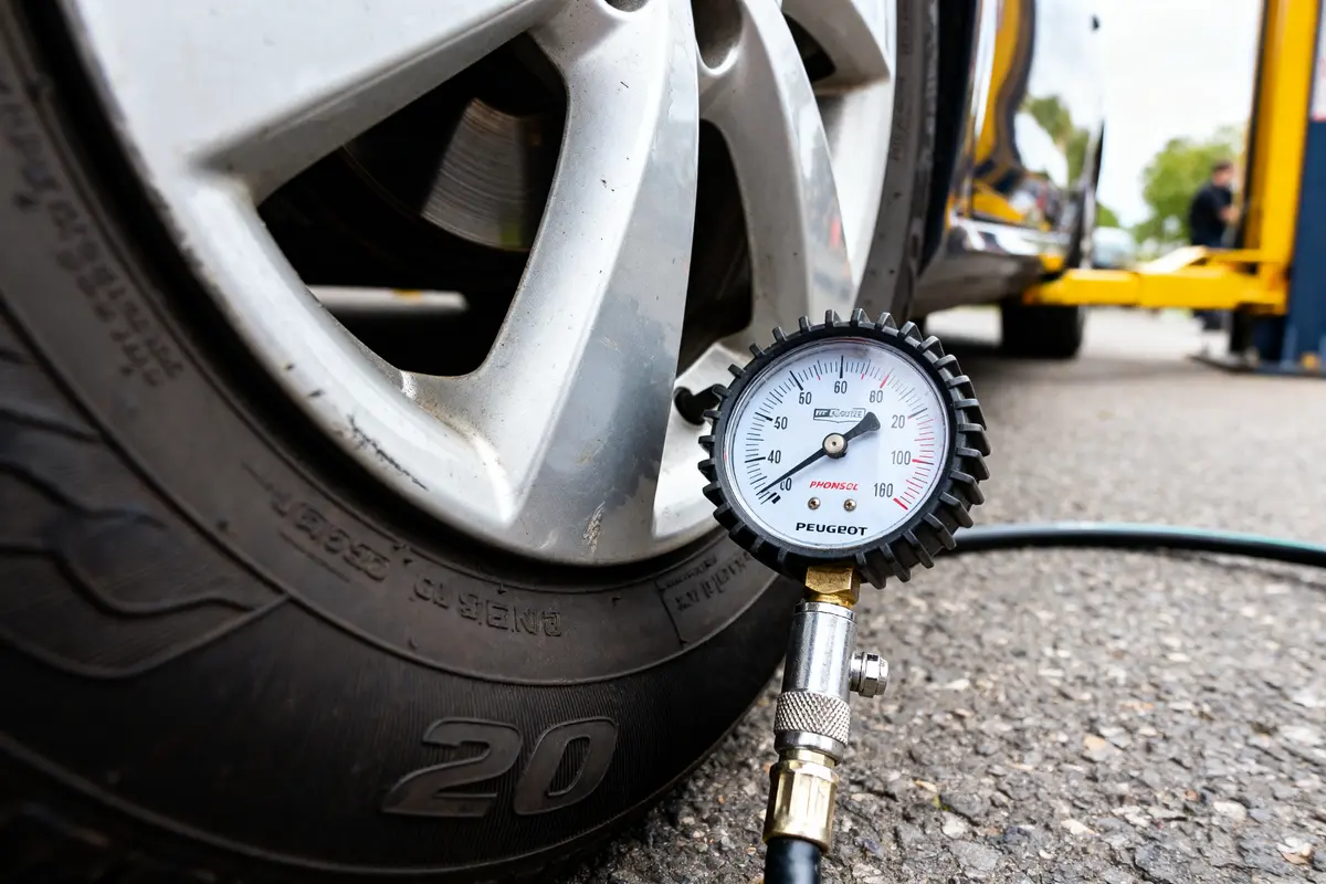 Manomètre mesurant la pression d'un pneu de voiture sur un parking, gros plan sur jante et manomètre.