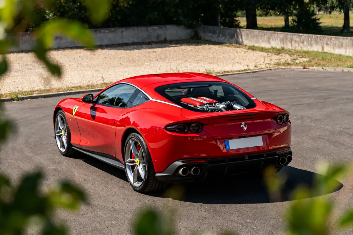 Ferrari Roma rouge garée sur une route, vue arrière, moteur visible sous vitre