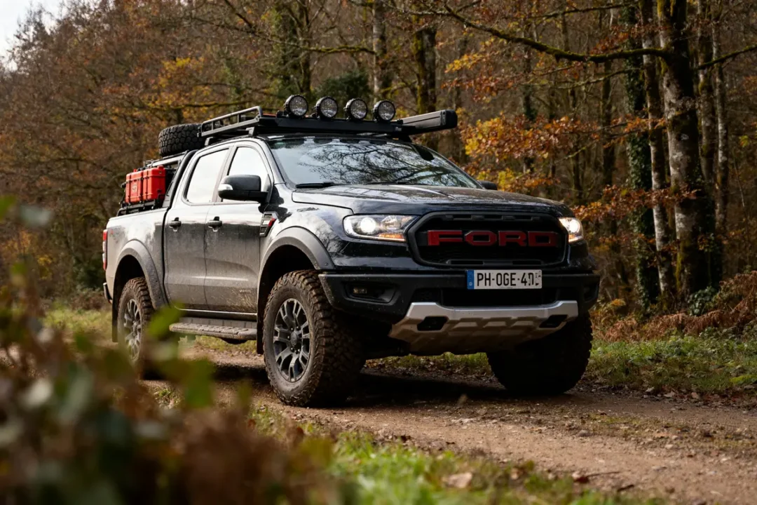 Pickup noir Ford Ranger Raptor sur chemin forestier automnal avec équipements tout-terrain supplémentaires
