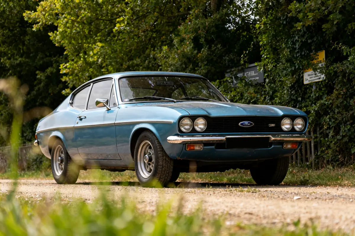 Voiture classique Ford Capri 1970 bleue garée sur un chemin arboré en été