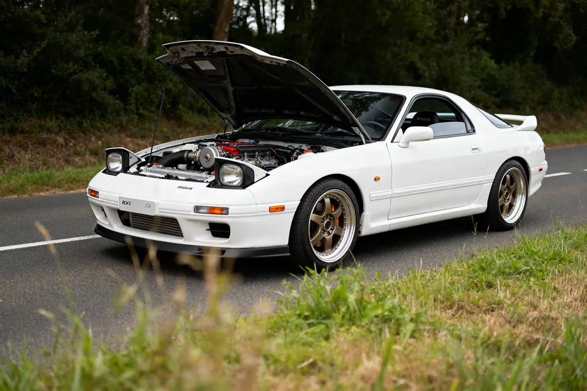 Mazda RX7 coupé blanc capot ouvert sur route entourée de verdure