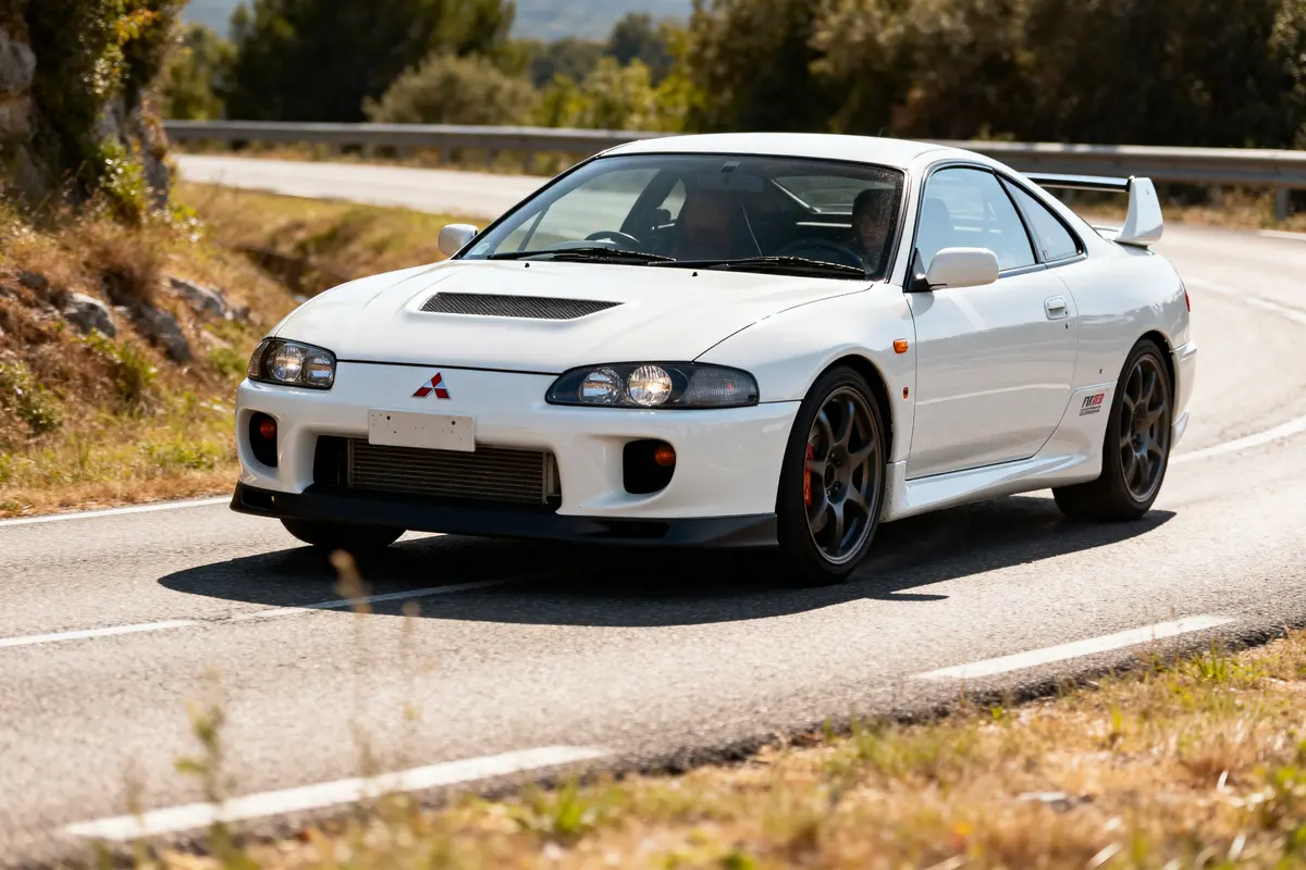Mitsubishi FTO coupé blanc sur route sinueuse en pleine nature, côté conducteur visible