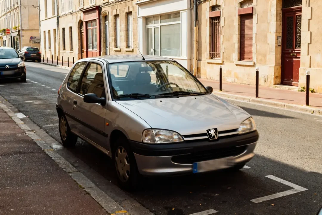 Peugeot 106 grise garée dans une rue bordée de bâtiments en pierre