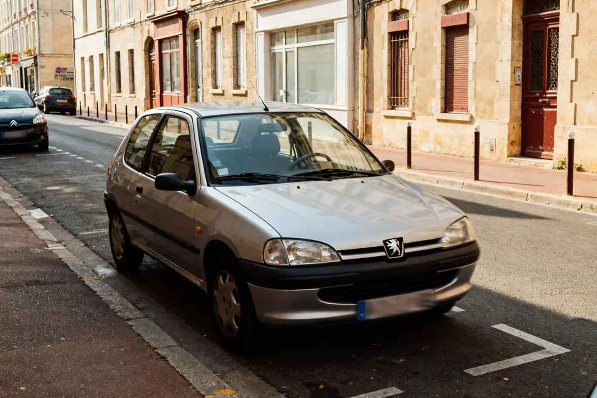 Peugeot 106 grise garée dans une rue bordée de bâtiments en pierre