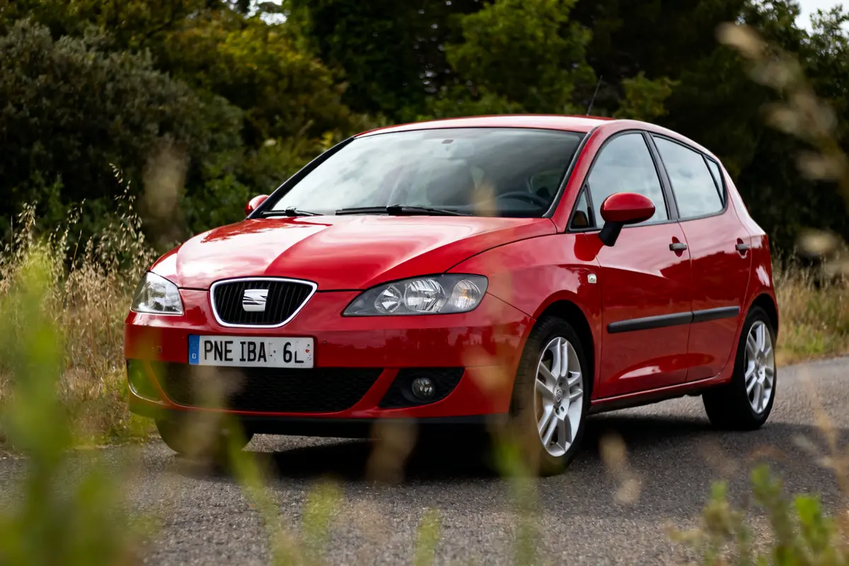 Voiture rouge SEAT Ibiza 6L garée sur route avec végétation en arrière-plan