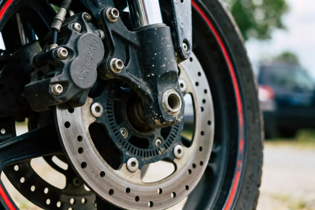 Gros plan sur disque et frein avant moto avec étrier noir et roue en arrière-plan
