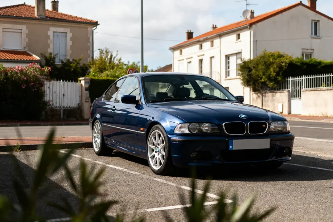 BMW E46 bleu garée devant des maisons de style traditionnel dans une rue résidentielle