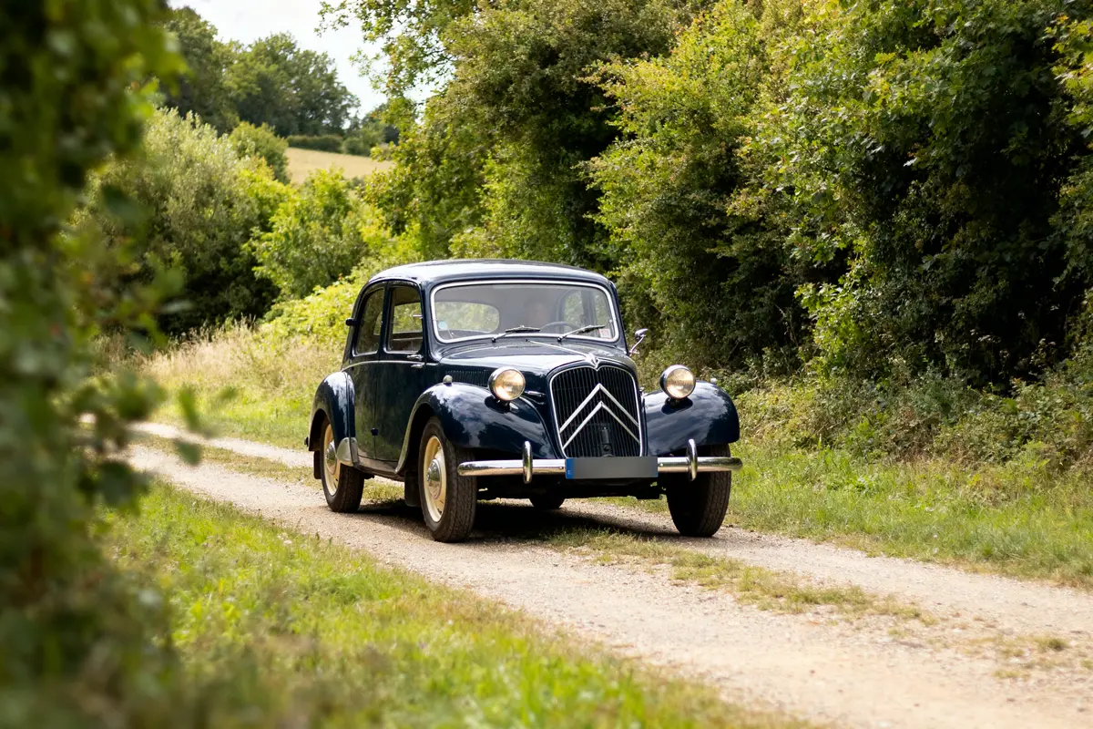 Citroën Traction Avant sur chemin de campagne entourée de verdure et arbres luxuriants