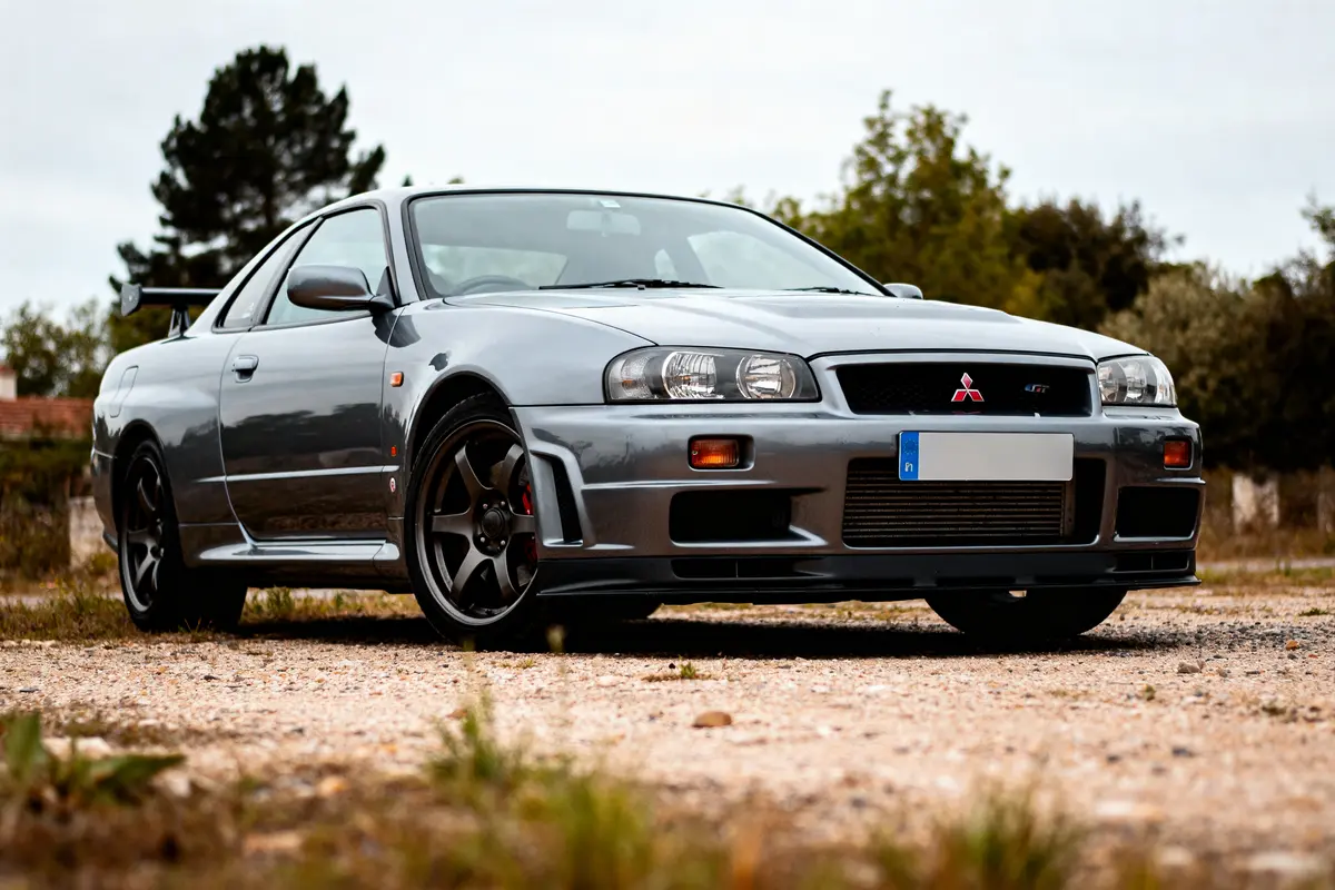 Voiture sport Mitsubishi GTR grise stationnée sur sol gravier devant arbres et ciel nuageux