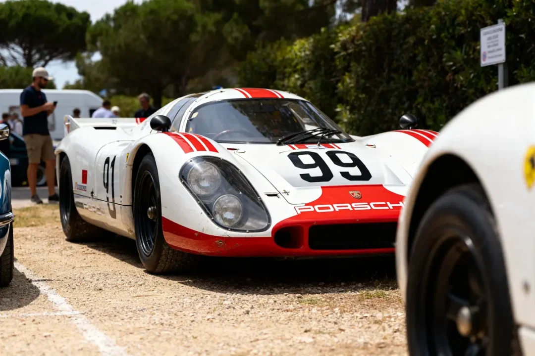 Voiture de course Porsche 917 blanche et rouge numéro 99 sur piste gravelée.