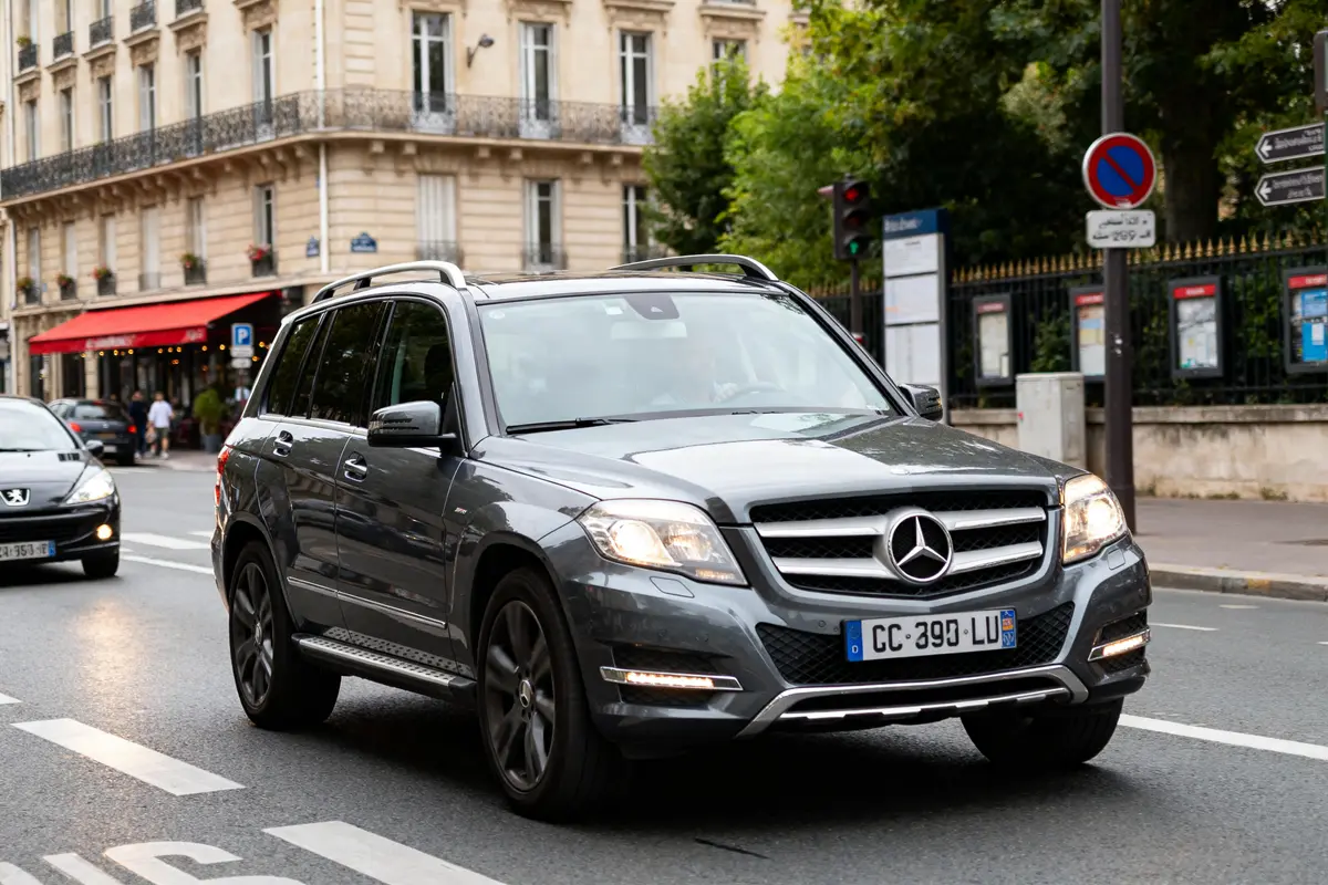 SUV Mercedes GLK gris circulant en ville devant un bâtiment historique et feu tricolore