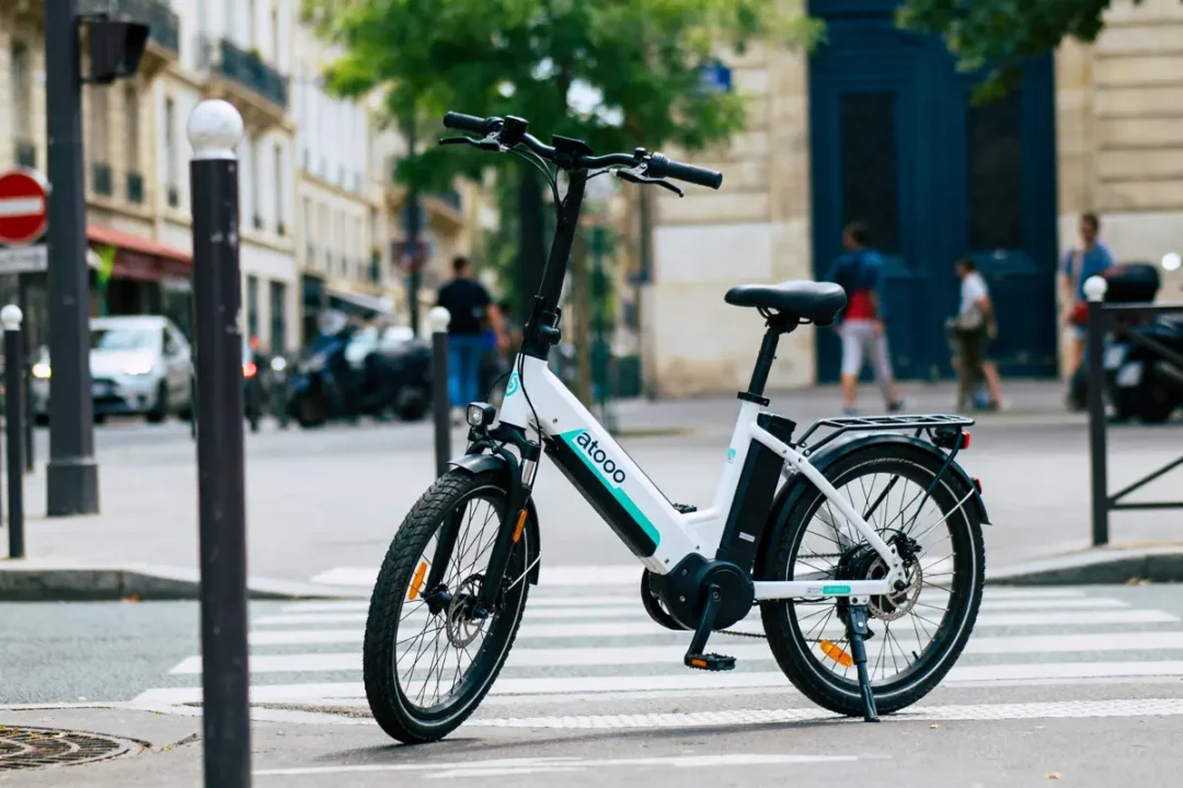 Vélo électrique blanc stationné sur passage piéton en milieu urbain, arrière-plan flou de rue et piétons.