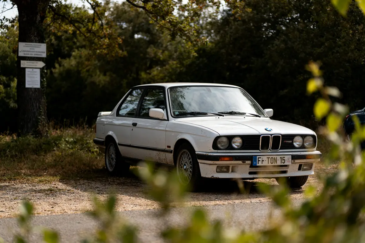 BMW blanche stationnée en nature, modèle classique blw e30, vue latérale avant