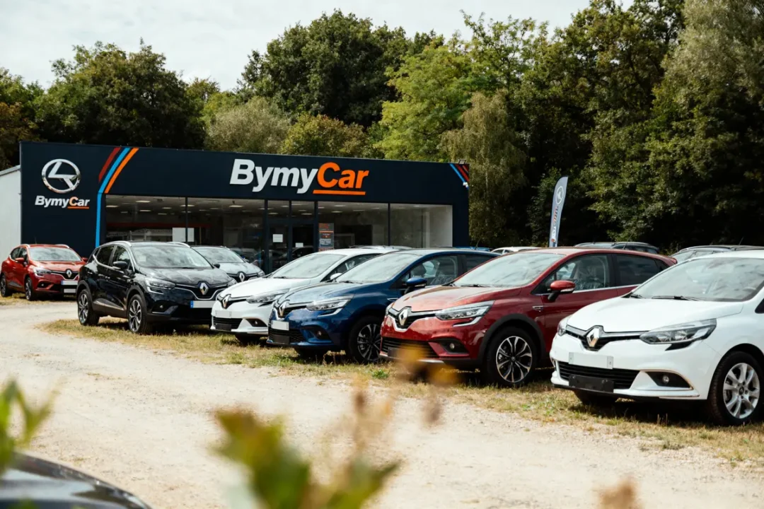 Concessionnaire BymyCar avec des voitures Renault garées à l'extérieur, entourées de verdure.
