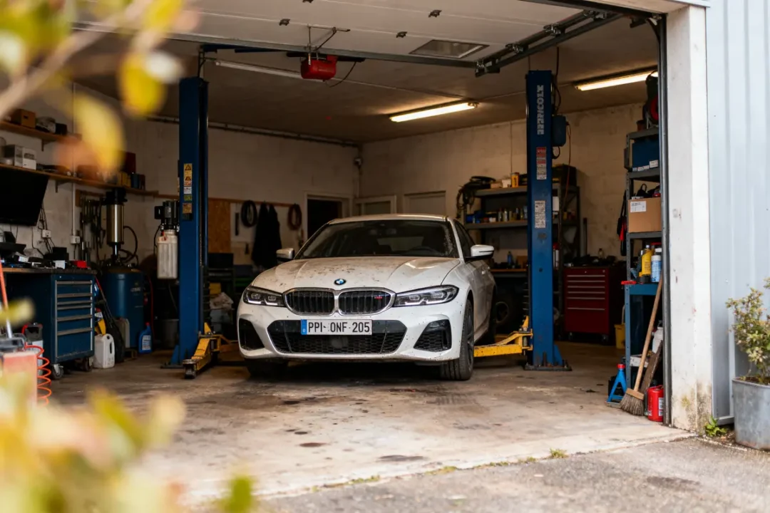 Voiture blanche dans un garage sur un pont élévateur, équipée pour entretien mécanique.