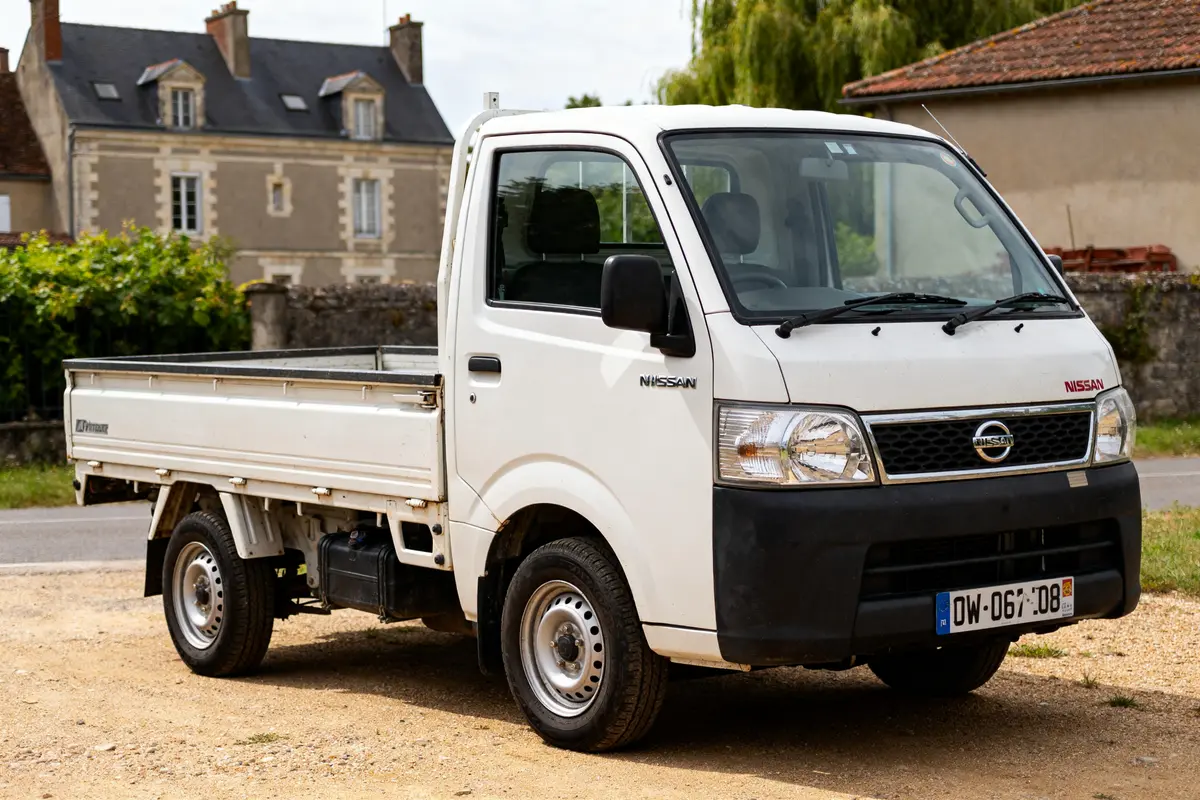 Utilitaire Nissan blanc garé devant une maison ancienne en arrière-plan