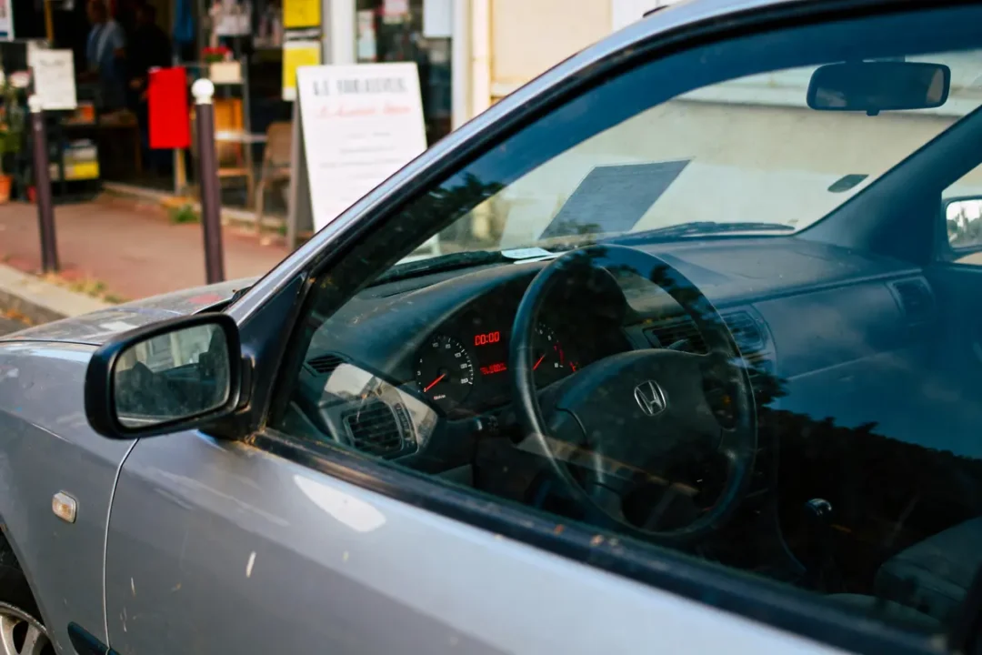 Vue intérieure d'une voiture, volant Honda, tableau de bord allumé, environnement extérieur flou.