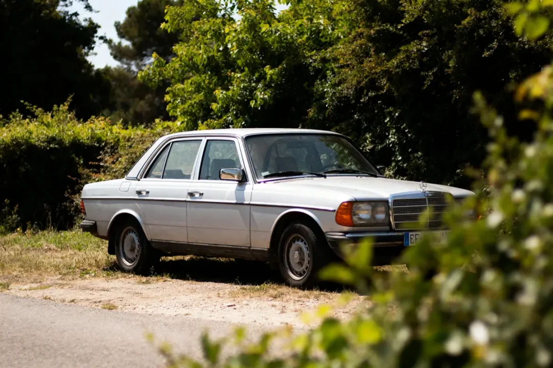Voiture classique blanche garée sur chemin rural, entourée de verdure luxuriante.